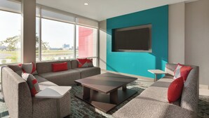A modern living room with a sectional sofa, a coffee table, and a flat-screen TV mounted on a teal wall. - avid hotel Byron Warner Robins by IHG (Byron)