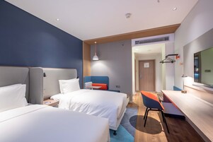 Una habitación de hotel con dos camas, un escritorio, una silla, un televisor y una puerta que da a otra habitación.
