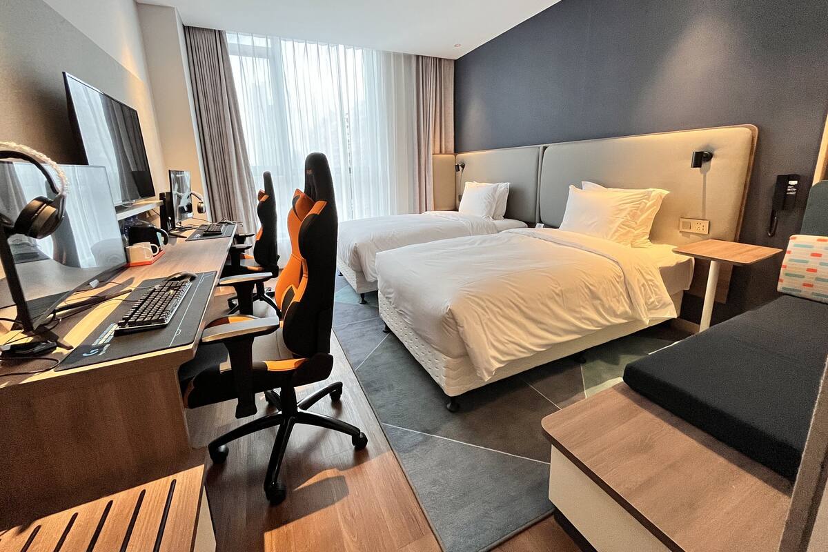 Ein Hotelzimmer mit Schreibtisch, zwei Betten, einem Sessel, einem Fernseher und einem Telefon.