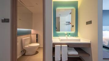A modern bathroom with a toilet, sink, and mirror. There are towels hanging on a rack and a shelf with toiletries.