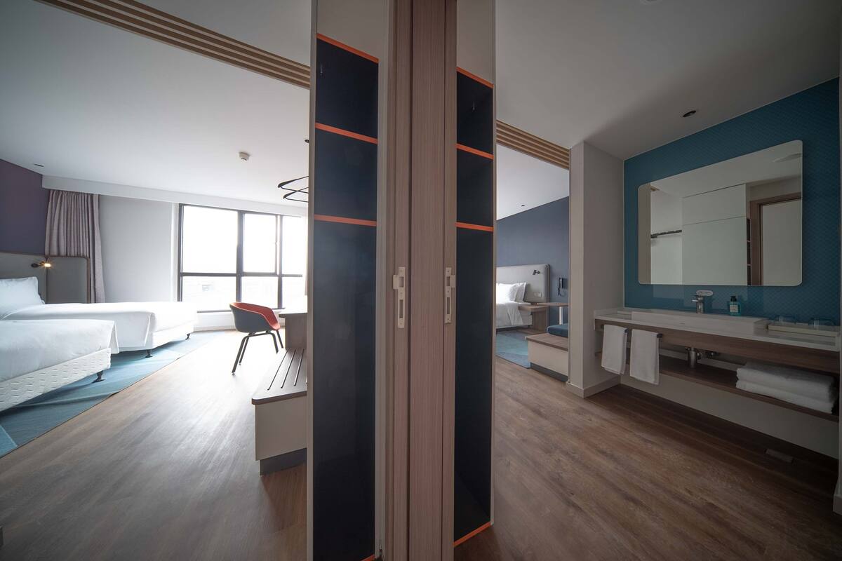Ein modernes Hotelzimmer mit einem großen Bett, einem Schreibtisch, einem Stuhl, einem Badezimmer mit Spiegel und Blick auf die Stadt.