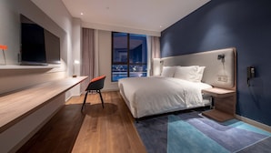 A modern hotel room with a large bed, a desk, a flat-screen TV, and a view of the city at night. - Holiday Inn Express Nantong North Gateway by IHG (Nantong)