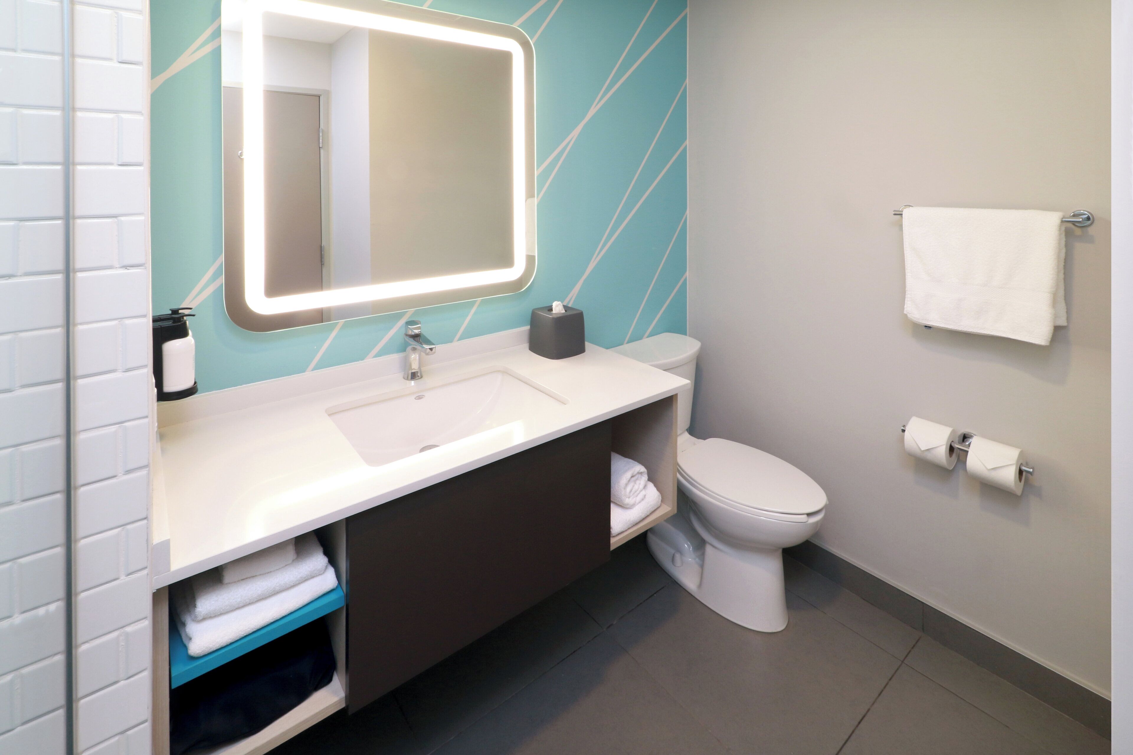 A modern bathroom with a white sink, a mirror with built-in lighting, a toilet, and a towel rack.