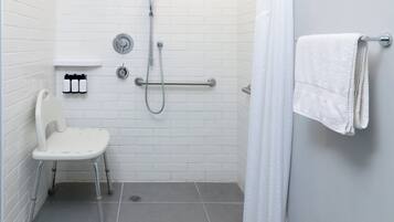 Un baño con inodoro blanco, ducha con cabezal de ducha de mano, barra de apoyo y perchero.