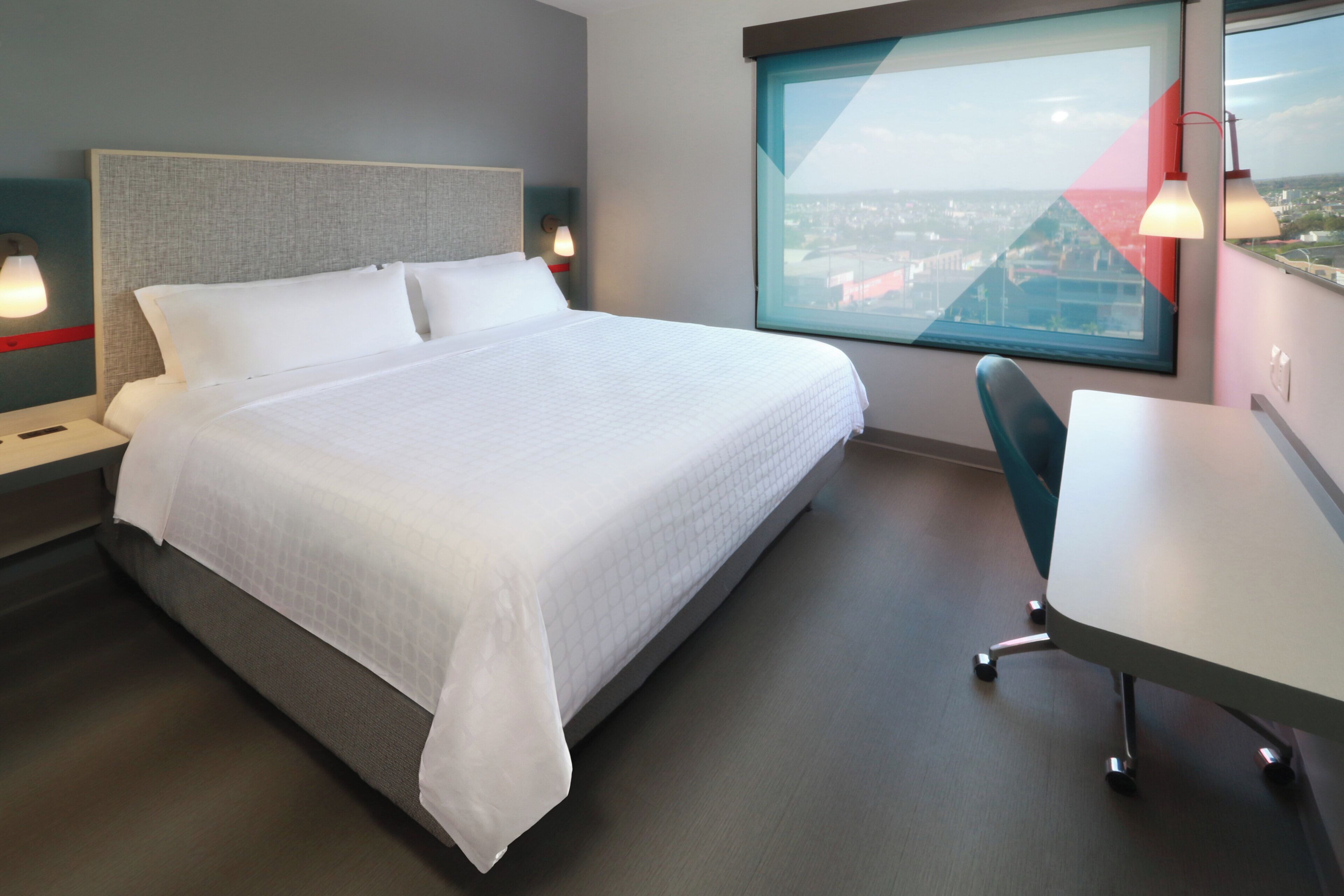 A modern hotel room with a large bed, a desk, and a city view.