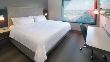 A modern hotel room with a large bed, a desk, and a city view.