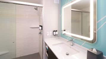 A modern bathroom with a glass-enclosed shower, a white sink with a mirror, and toiletries on the wall.