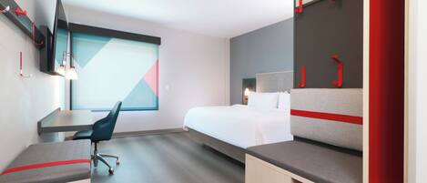 Una habitación de hotel moderna con una cama, escritorio, silla y televisor montado en la pared.