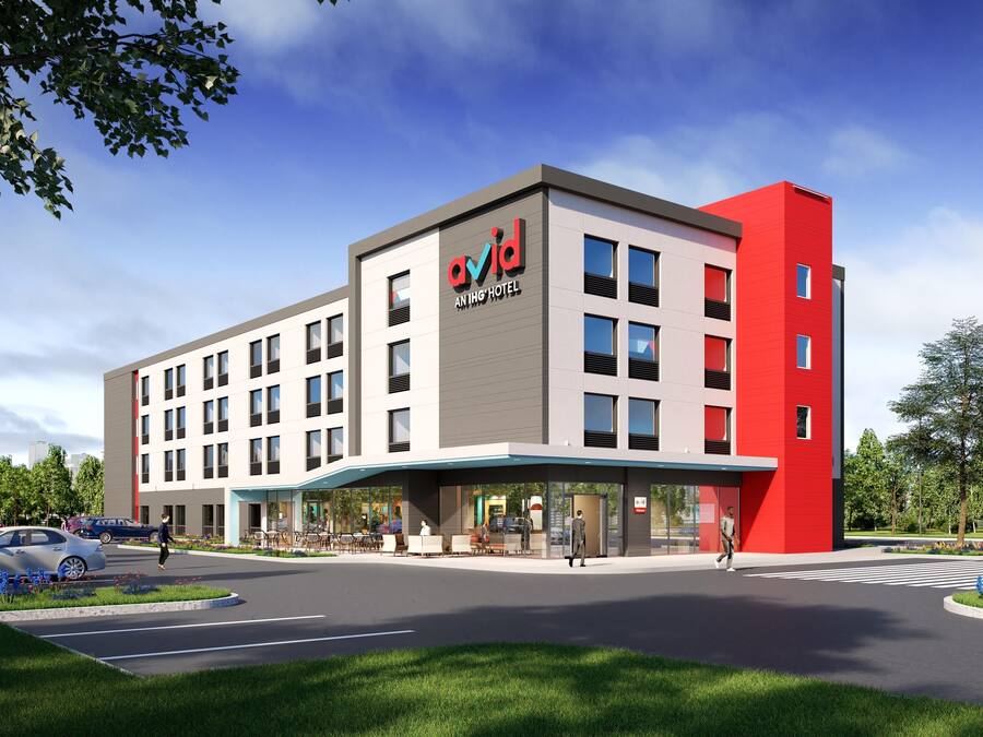 A modern hotel building with a prominent red and grey facade, multiple windows, and a covered entrance area.
