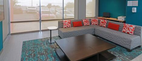 A modern living room with a grey sectional sofa, a small round table, and a large window with a view of parked cars.