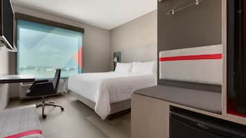 A hotel room with a bed, desk, chair, and a small kitchenette.