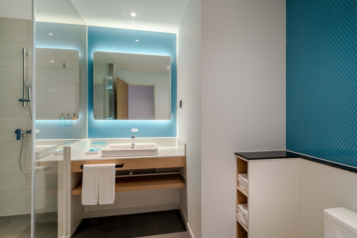 A modern bathroom with a glass shower enclosure, a white sink with a mirror above it, and a blue accent wall.