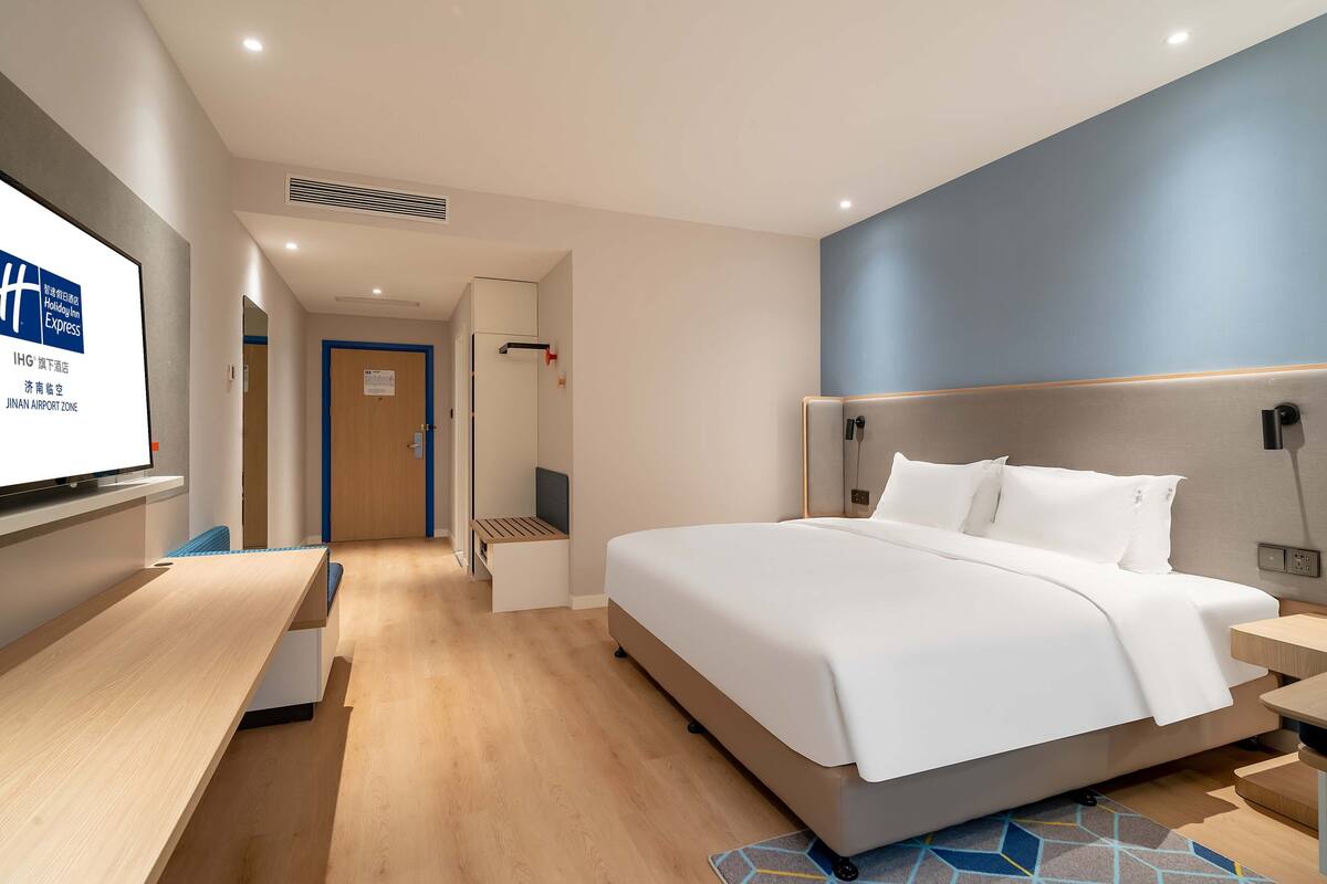 A modern hotel room with a large bed, a desk, and a television on the wall.
