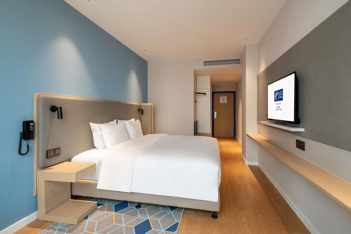 A hotel room with a bed, bedside table, and a mounted TV.