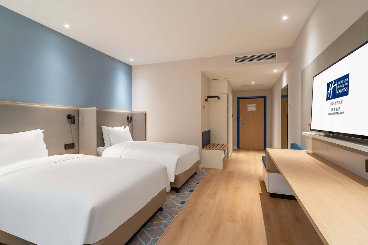 A hotel room with two beds, a desk, and a television screen displaying the hotel's name.