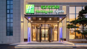 Entrada de un hotel Holiday Inn Express con puerta giratoria, señalización iluminada y fachada moderna.