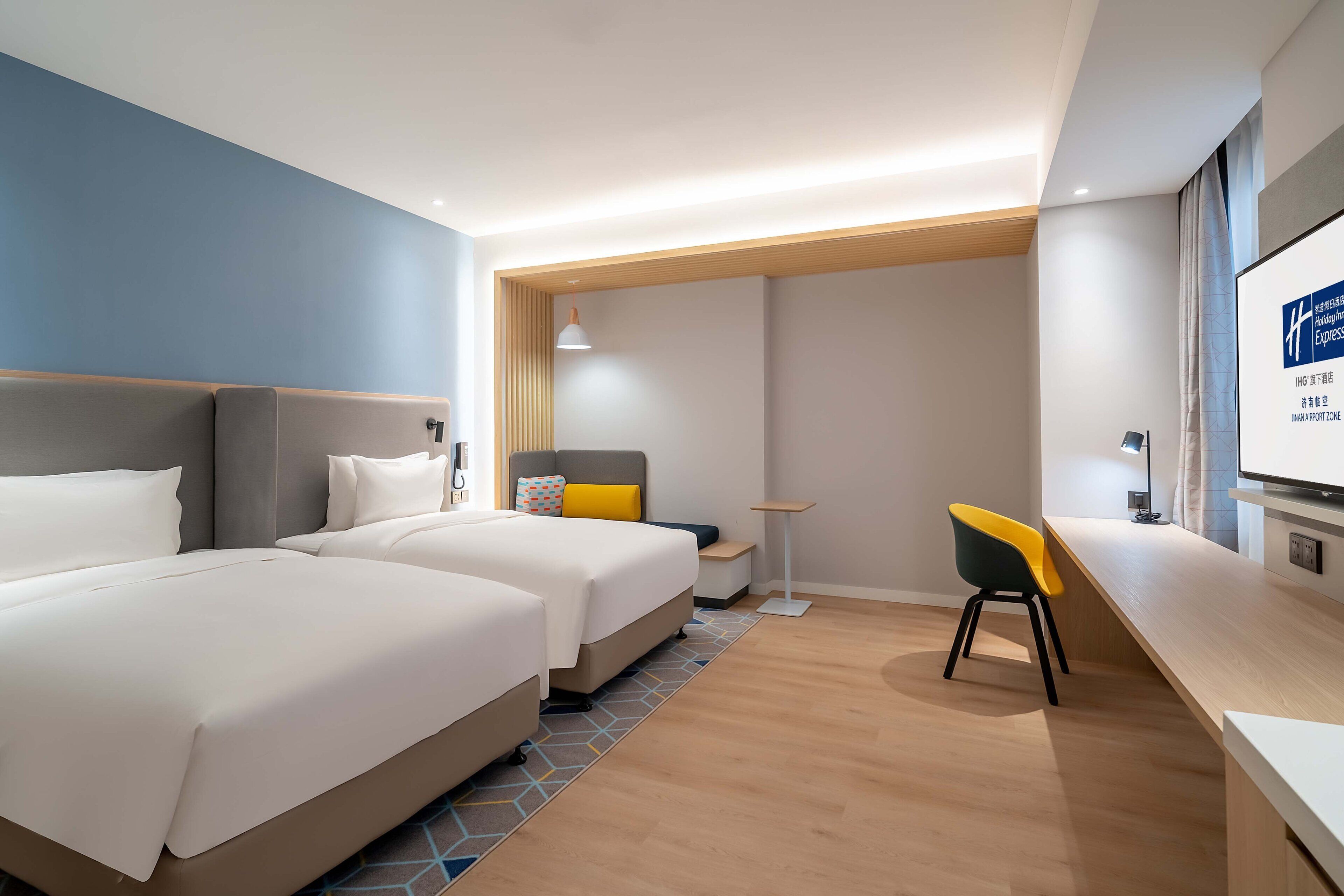 Ett hotellrum med två sängar, ett skrivbord, en stol, en tv och ett fönster med gardiner.