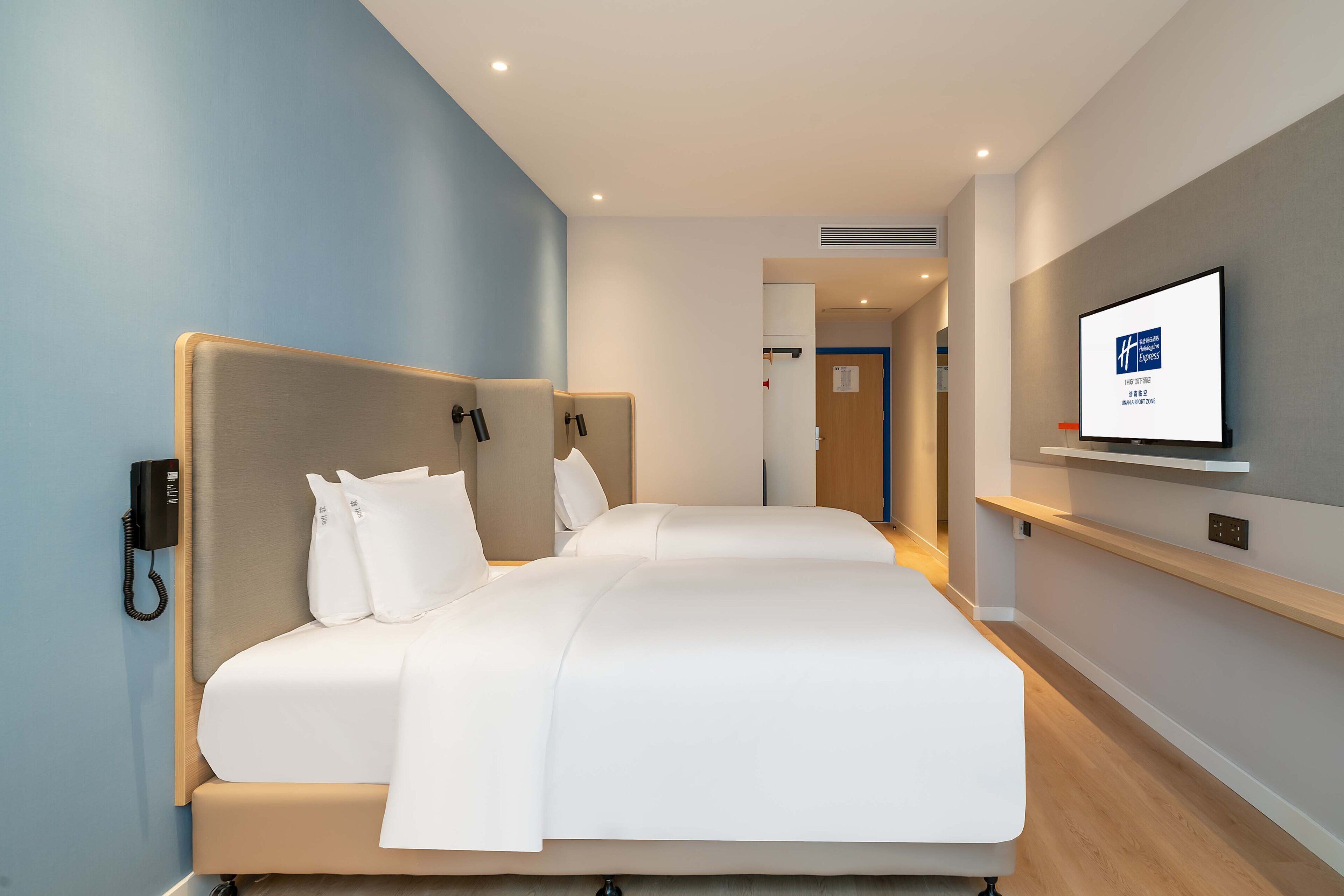 A modern hotel room with a large bed, a mounted TV, and a phone on the wall.