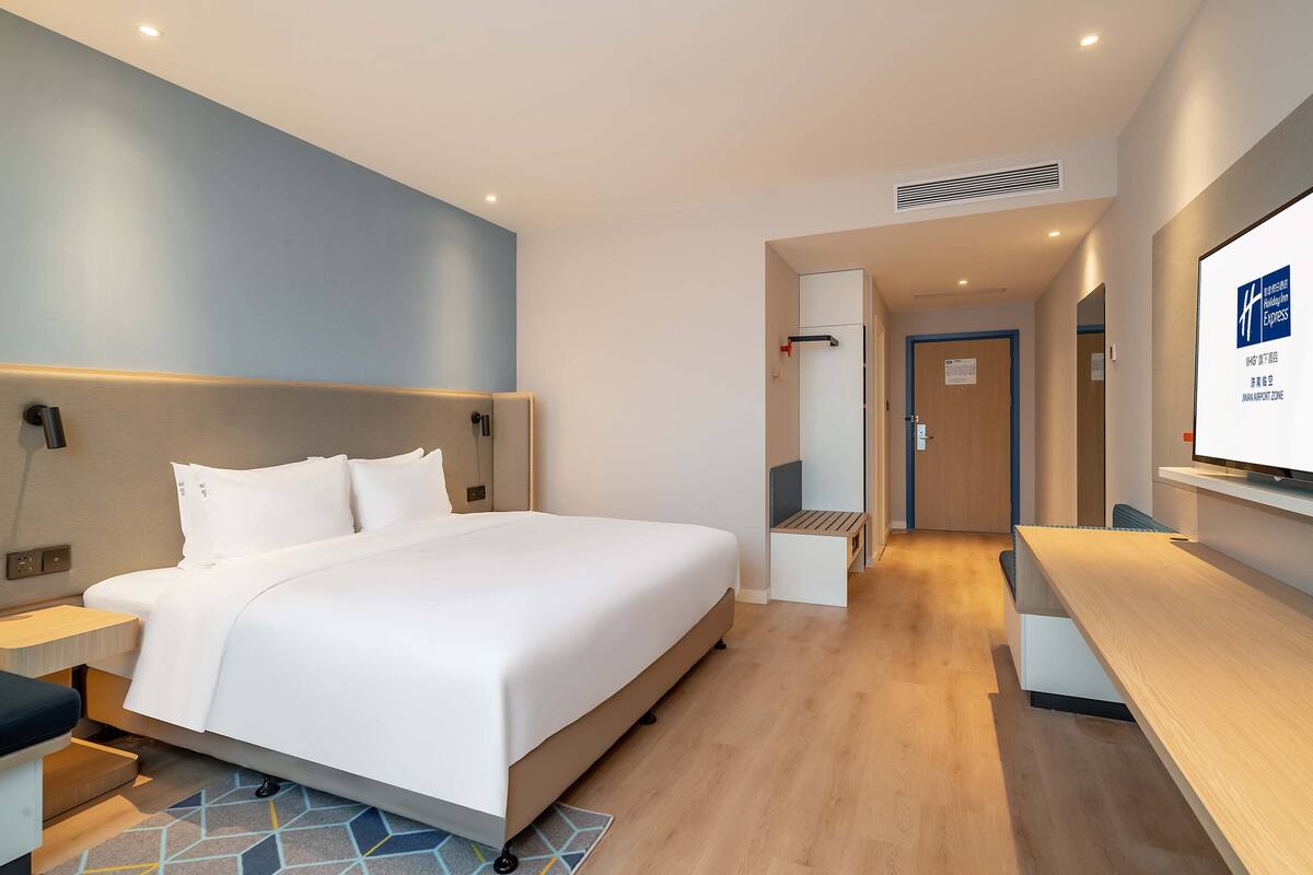 A modern hotel room with a large bed, a desk, and a television.