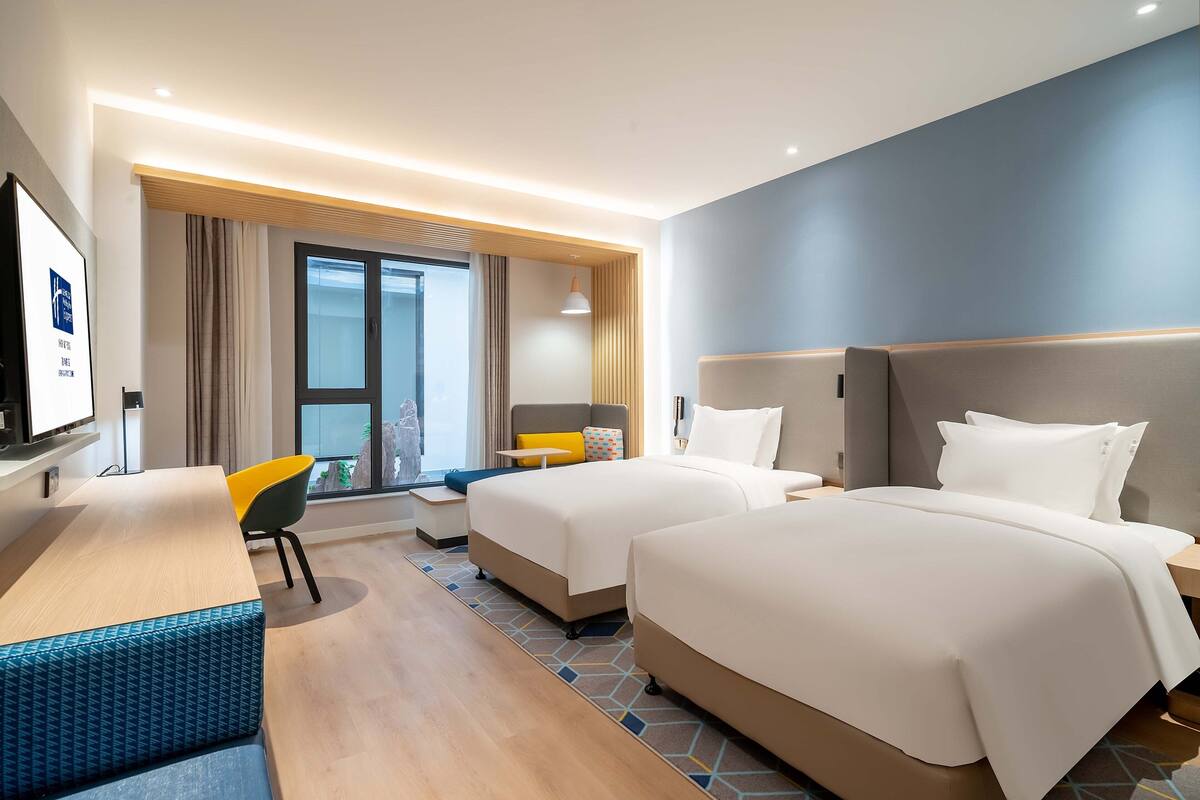 A modern hotel room with two beds, a desk, and a chair.