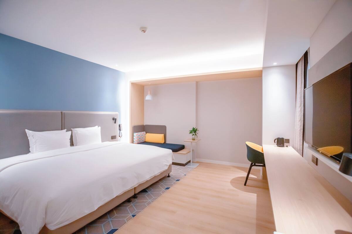 A modern hotel room with a large bed, a desk, and a TV.