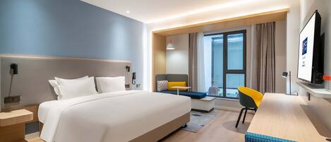 A modern hotel room with a large bed, a desk, a chair, and a TV.