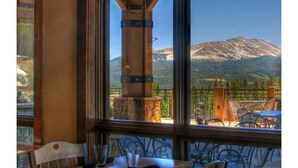 Un restaurante con vistas a la montaña, que cuenta con un pilar de piedra, mesas de madera y sillas de metal.