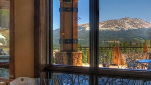 A restaurant with a mountain view, featuring a stone pillar, wooden tables, and metal chairs.