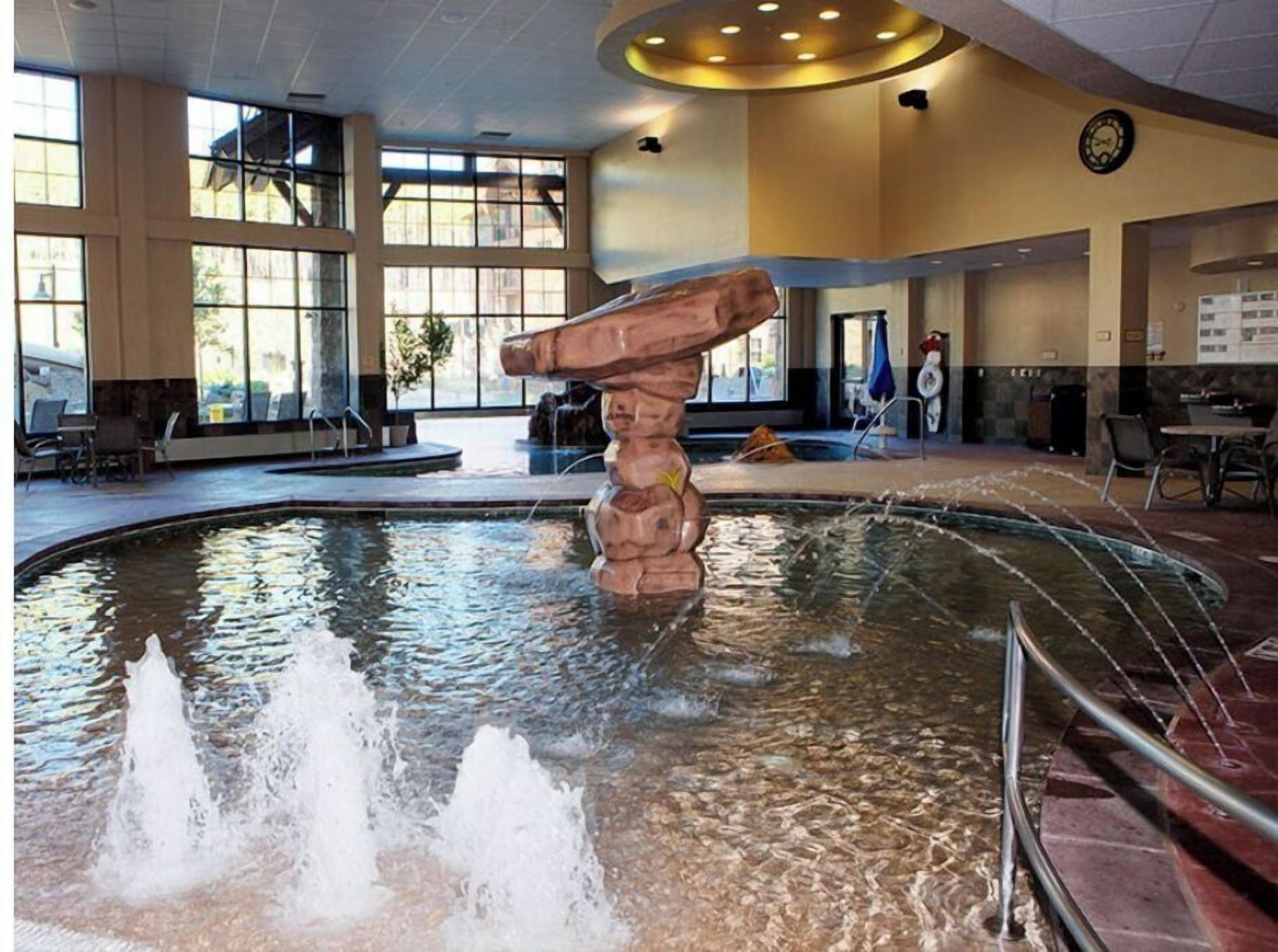 Une piscine dotée d’une structure rocheuse originale en son centre, entourée d’espaces de détente et de grandes fenêtres.