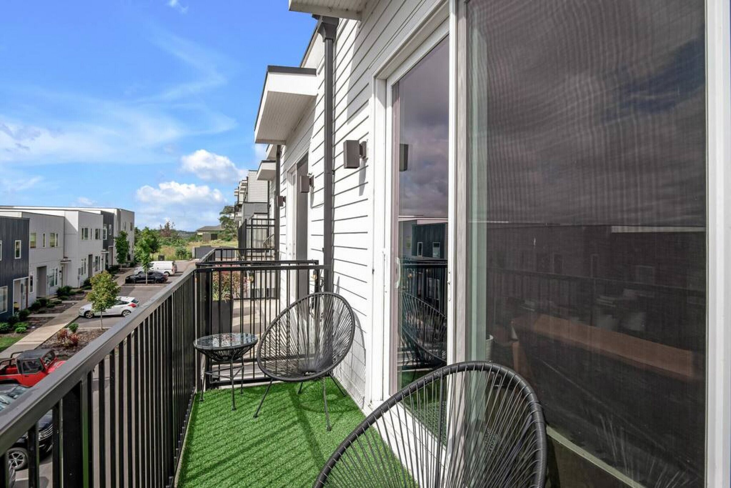 A balcony with two chairs, a small table, and a view of neighboring houses.