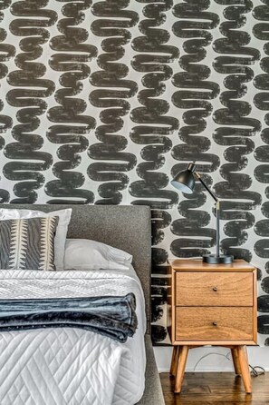 A neatly made bed with a quilted cover, a bedside lamp, and a wooden nightstand with drawers. - Skyline View, Garage, Mural and Ping Pong in Big Modern Home (Nashville)