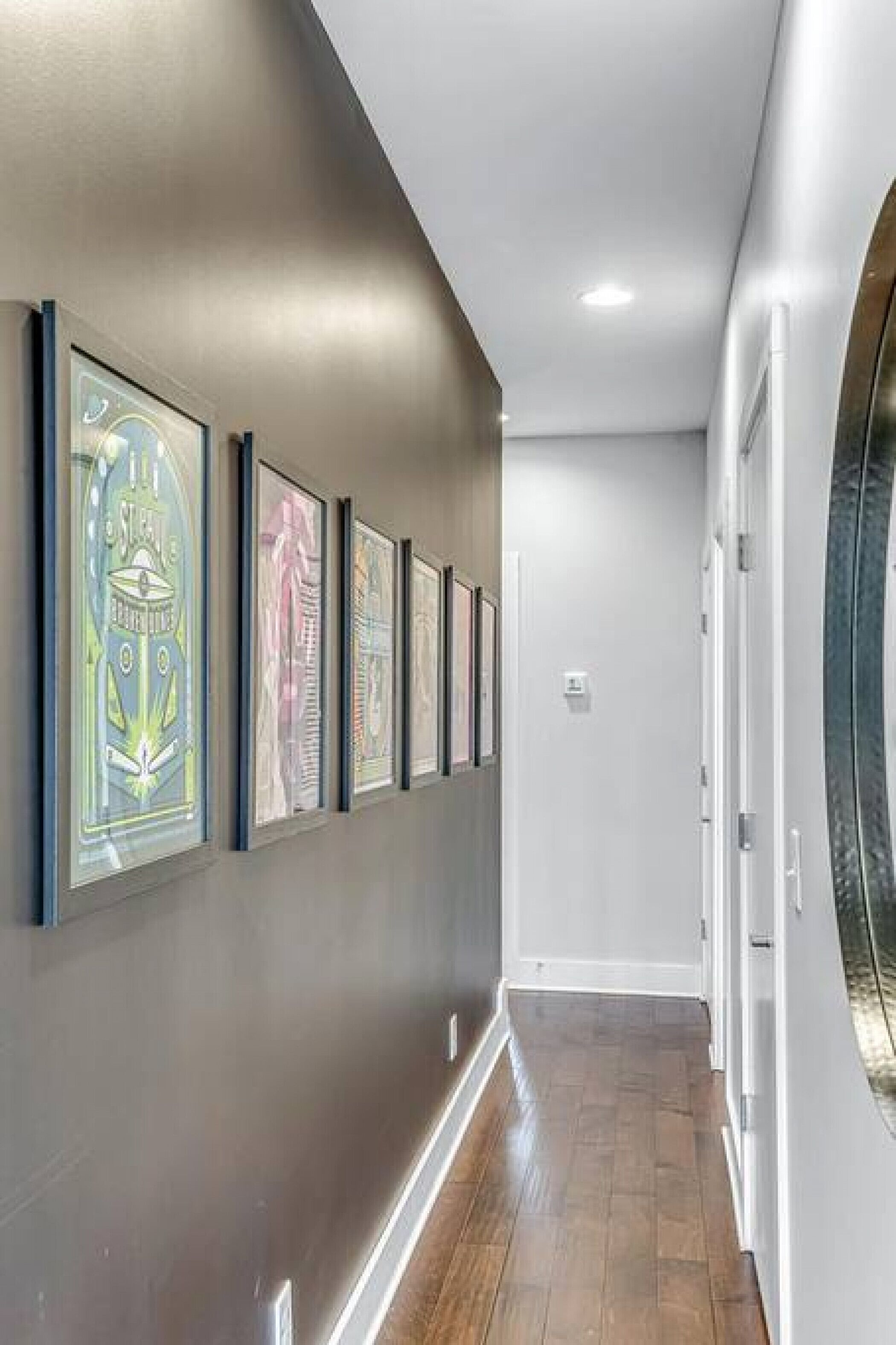 A hallway with framed artwork on the wall, a wooden floor, and a white door at the end.