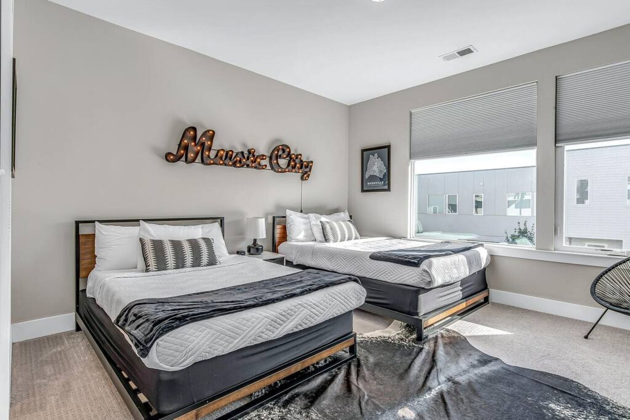 A modern bedroom with two beds, a large wall-mounted sign, and a window with blinds.