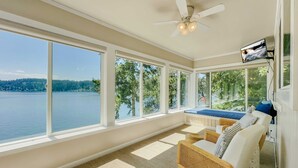 Una veranda con ampie finestre che si affacciano su un lago, una ventola a soffitto e un televisore montato a parete.