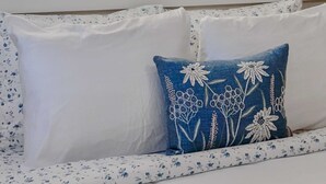 Una stanza con una grande finestra che si affaccia su un lago e una foresta, un divano bianco con cuscini floreali e una lampada a soffitto.