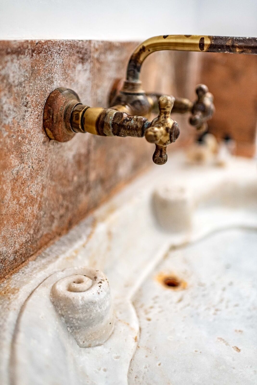 A close-up of a vintage brass faucet with a curved spout, attached to a textured wall.
