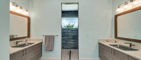 A modern bathroom with two sinks, a large mirror, and a view through a glass door to an outdoor area.