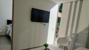 A modern living room with a flat-screen TV mounted on the wall, a small table with a plant, and a sofa with patterned cushions. - Apartamento (Medellín)