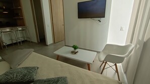 A living room with a sofa, a coffee table, a TV mounted on the wall, and a door leading to another room. - Apartamento (Medellín)