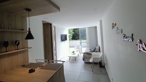 A modern kitchen with wooden cabinetry and a dining area with a table and chairs. There is a sofa and a TV in the living area. - Apartamento (Medellín)