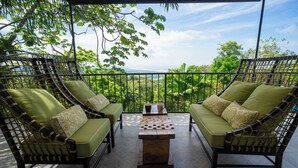 Un balcon agrémenté de meubles en osier et d’une table d’échecs, entouré d’une végétation luxuriante et offrant une vue dégagée sur le paysage.