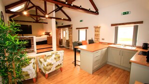 Una cocina acogedora con vigas de madera, una zona de comedor con mesa y sillas, y una cama al fondo.