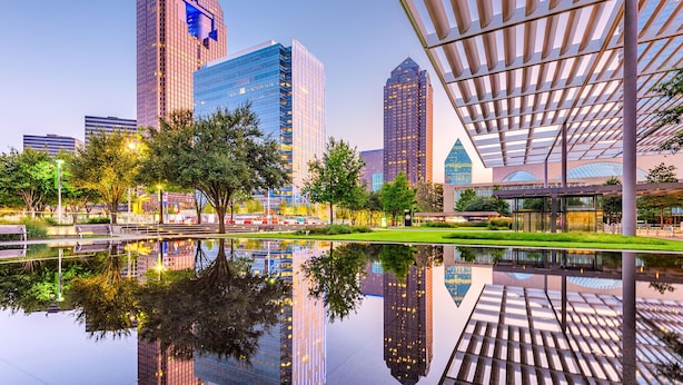 Een modern stadsplein met reflecterend water, hoge gebouwen en een bijzondere architecturale constructie met een gesloten dak.