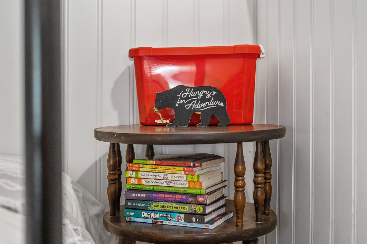 Une pile de livres sur une étagère en bois, avec un récipient rouge posé sur le dessus.