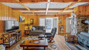 A cozy living room with wooden walls, a stone fireplace, a television, and comfortable seating. - South Shore Lake House Haven (Edinburg)