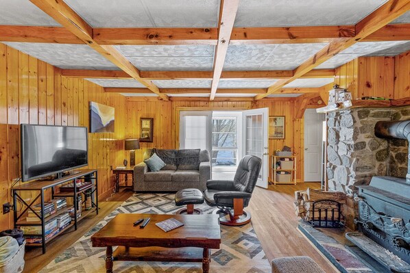 A cozy living room with wooden walls, a stone fireplace, a television, and comfortable seating.