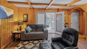 A cozy room with wooden walls and ceiling, a gray sofa, a black leather chair, and a small table with a lamp. - South Shore Lake House Haven (Edinburg)