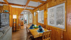 A wooden dining area with a table set for four, flanked by large windows with blinds, a stone fireplace, and a cozy living area with a sofa. - South Shore Lake House Haven (Edinburg)