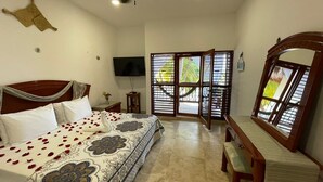 A bedroom with a bed, a desk, a chair, a ceiling fan, a TV, and a window with blinds. - Casa Pirata (Isla Holbox)