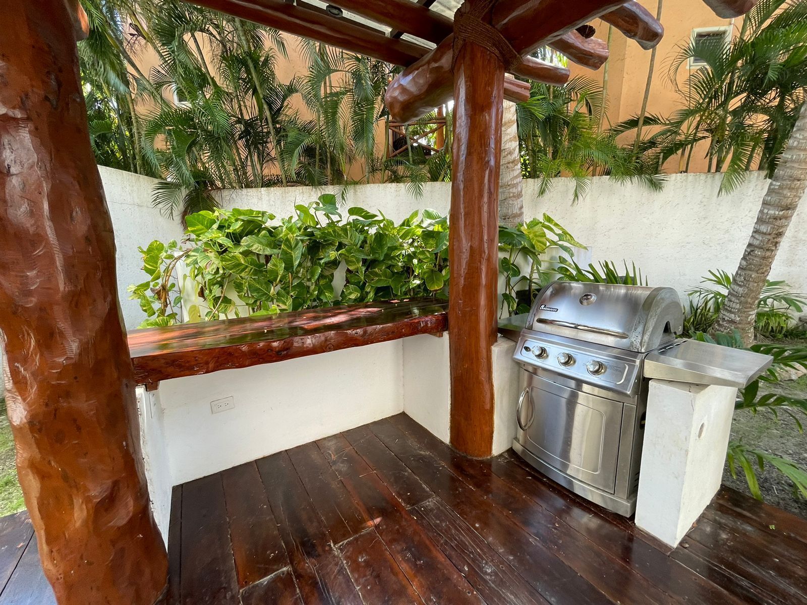 A patio area with a grill, wooden pergola, and lush greenery.